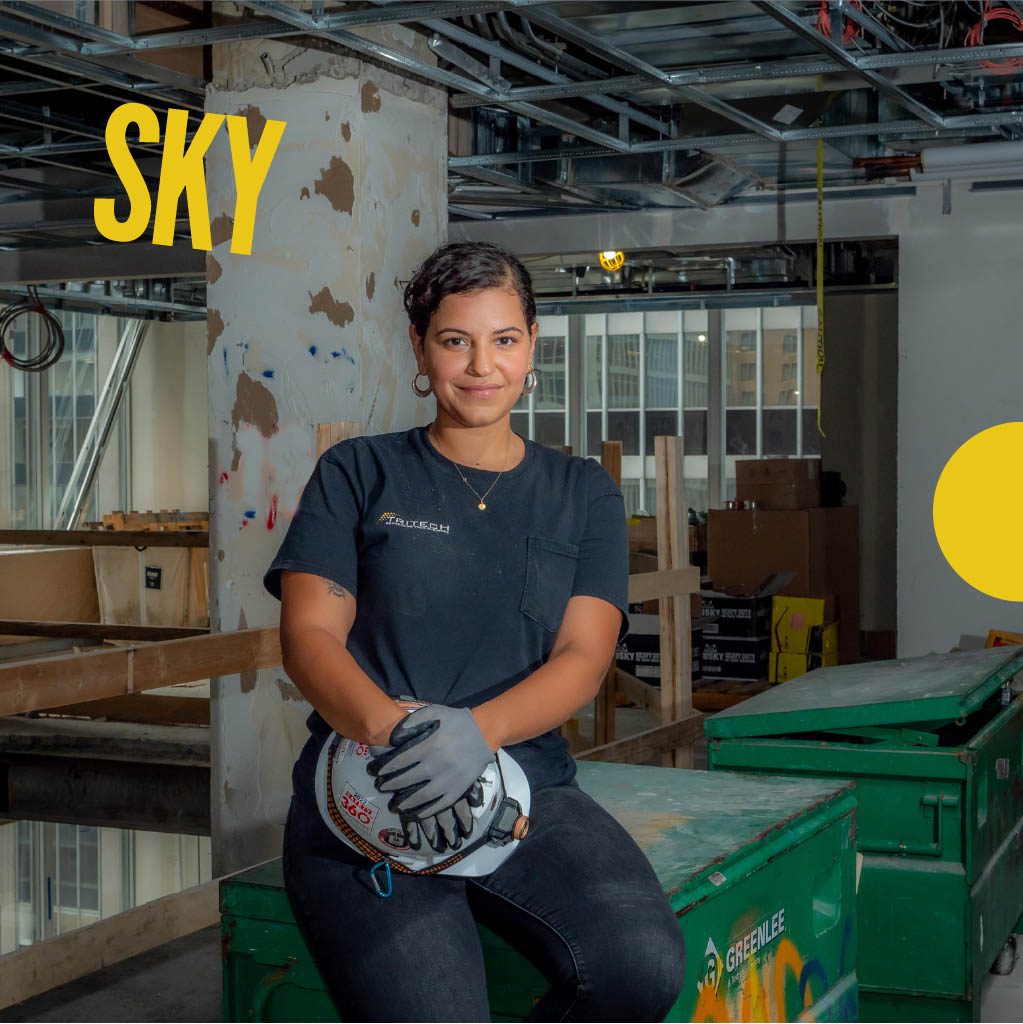 Photo of woman holding hard hat at work site. Name Sky in yellow font.